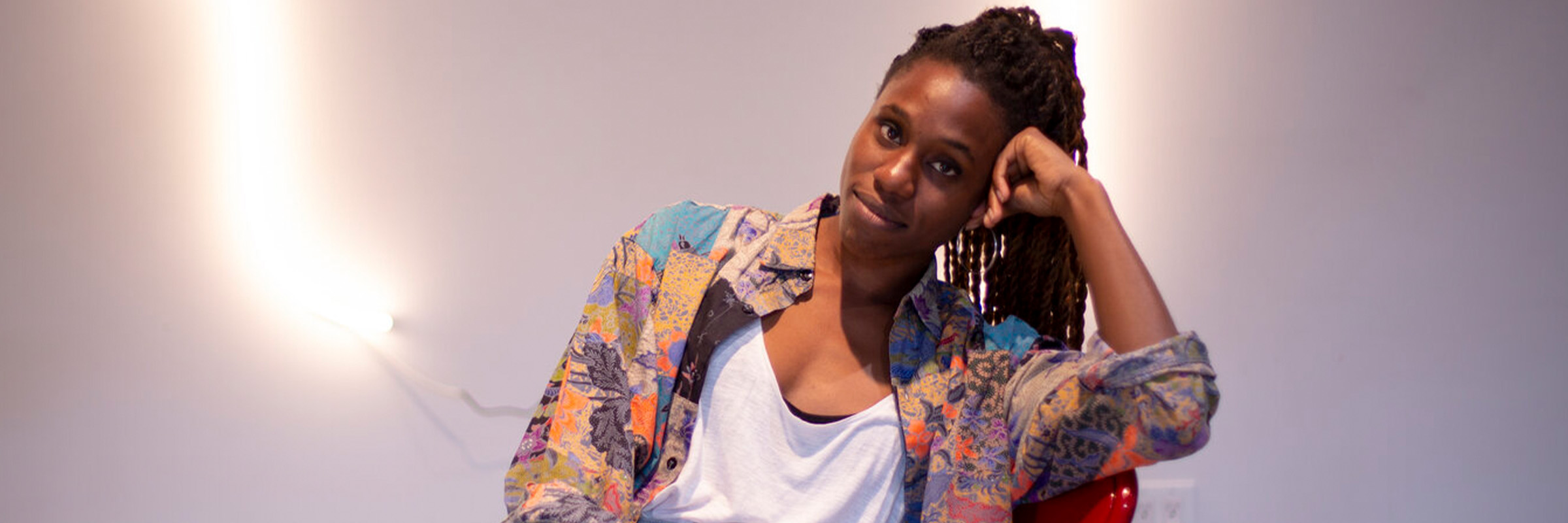 A portrait of Mimi Onuoha sitting in a red chair.