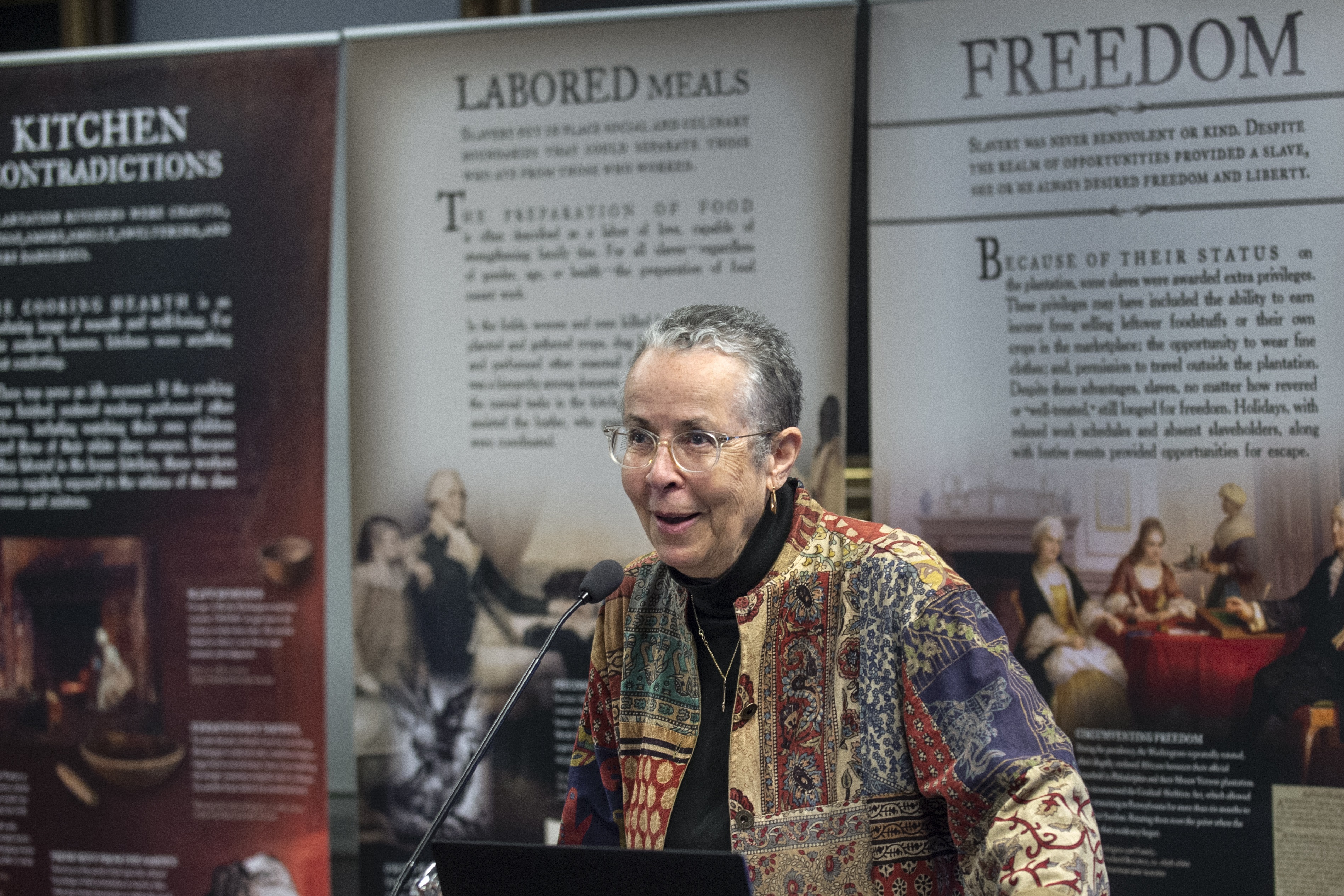 Leni Sorensen speaking at a podium in front of a backdrop of historical documents.