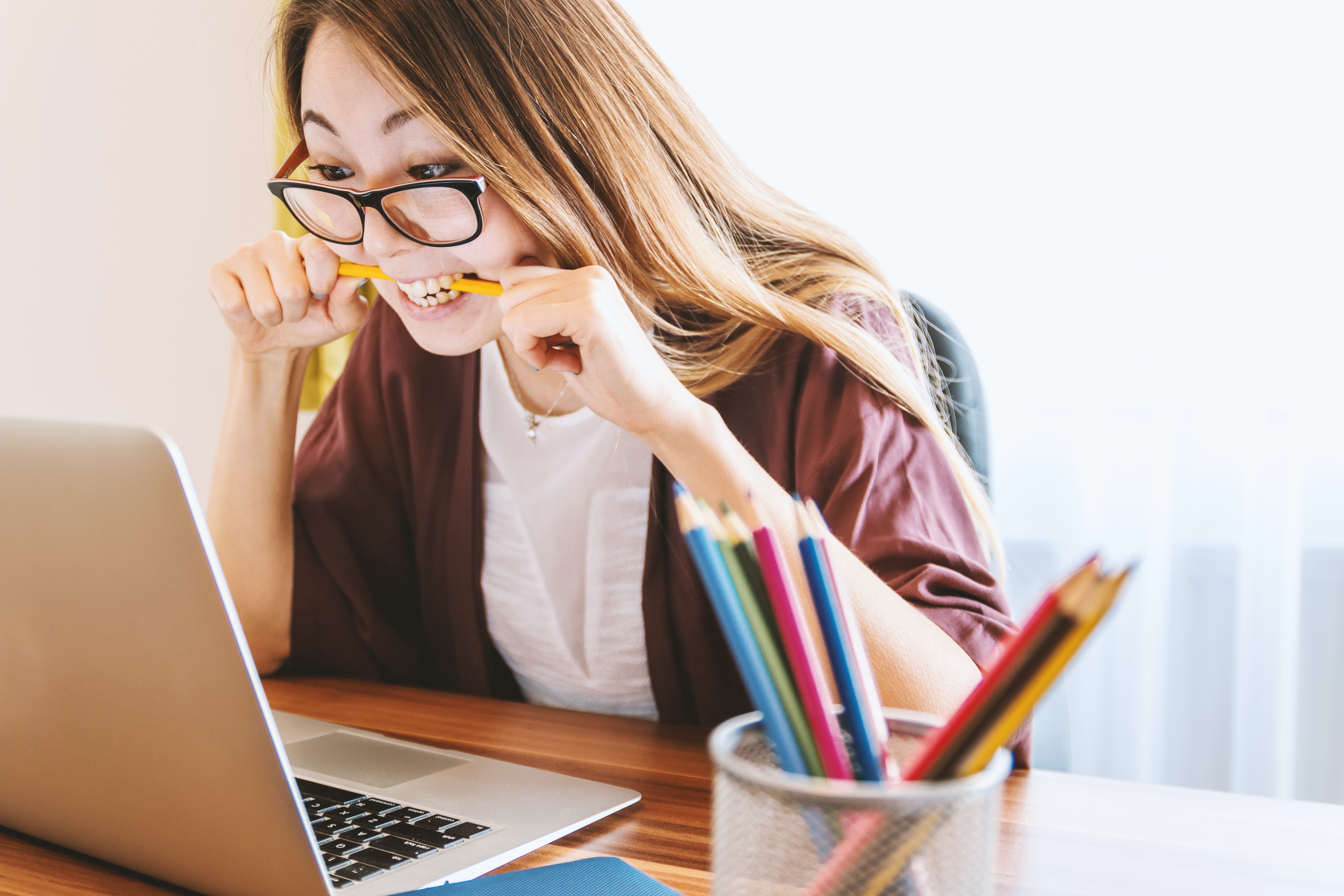 Woman biting a pencil while she looks at a laptop