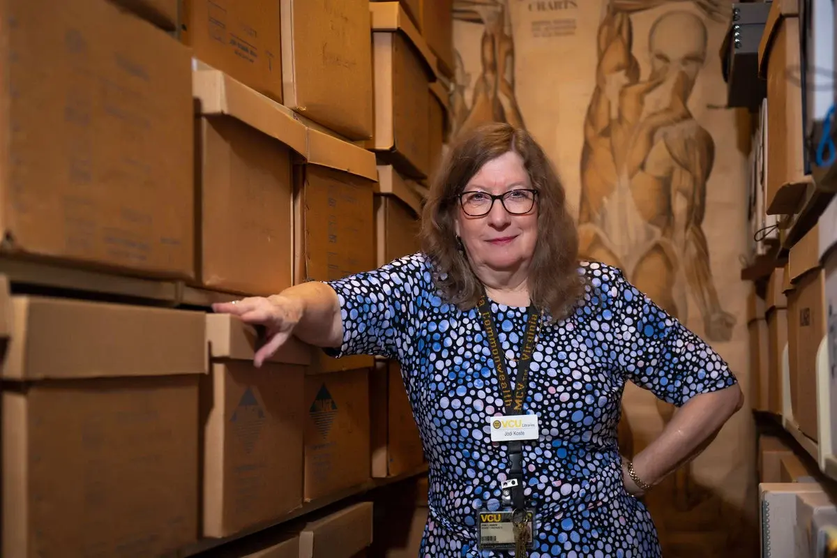 A portait of a woman from the waist up leaning against document boxes.