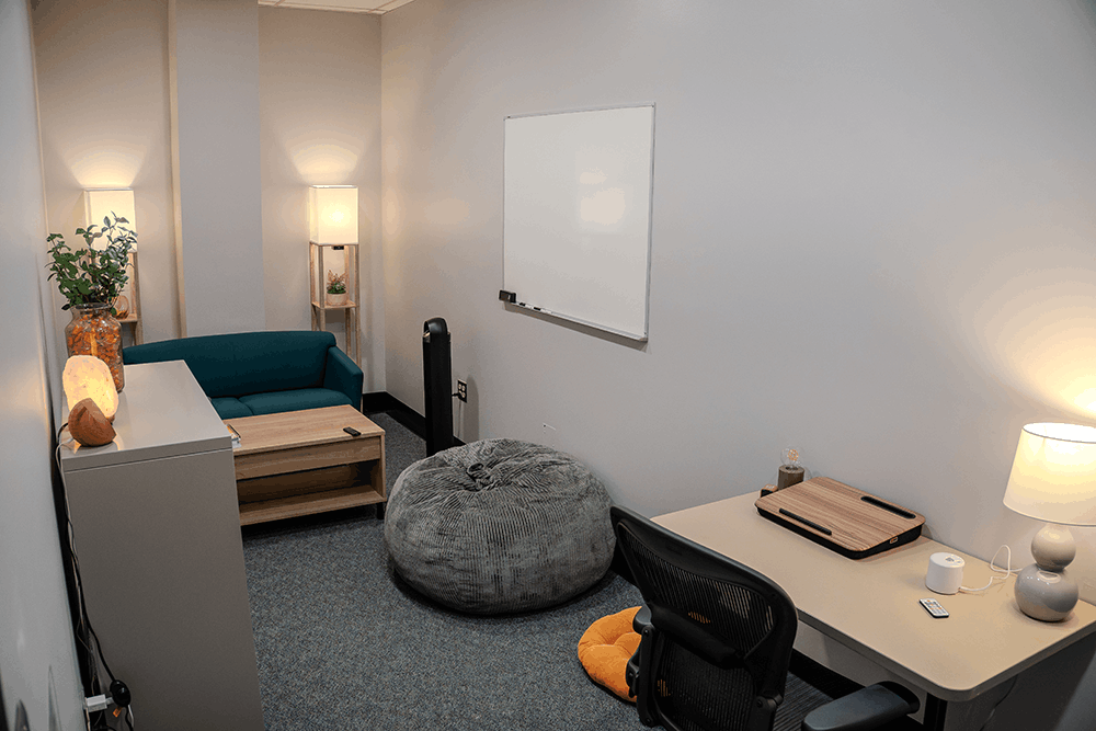 A small room with a desk at one end, 2 lamps and a sofa at the other end